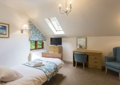 Bright single bedroom with skylight window, desk, armchair and soft furnishings creating a comfortable living space.