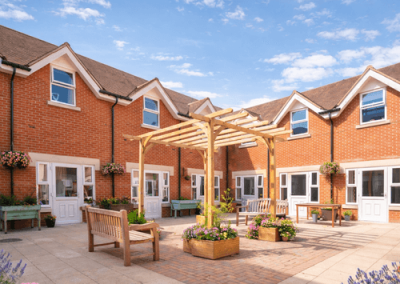 Enclosed courtyard garden with pergola seating, benches and well-maintained flower beds surrounded by brick buildings.