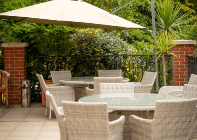 Outdoor patio area with wicker seating, large umbrella and greenery creating a relaxing dining space.