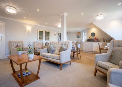 Bright communal lounge with armchairs, coffee table, television and soft furnishings creating a homely setting.
