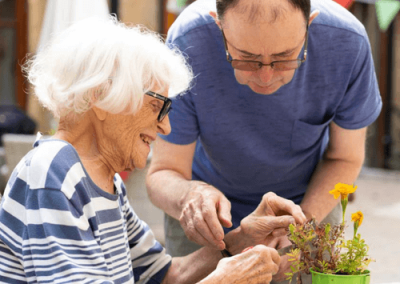 Resident and staff member planting flowers together during an outdoor gardening activity.