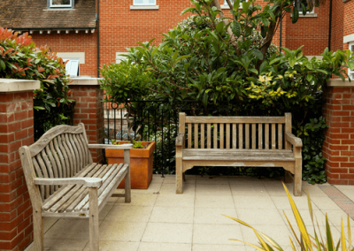 Patio seating area with wooden benches and planted borders within a secure courtyard garden.