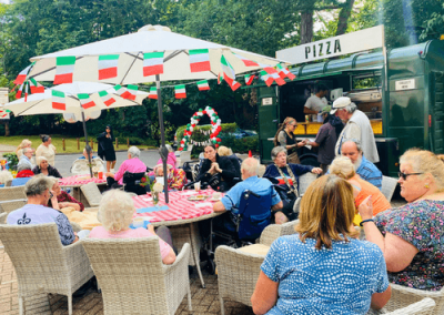 Residents enjoying a themed outdoor pizza event with decorated tables and food truck in the garden.