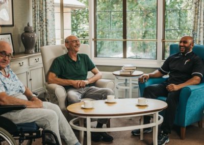 Residents and care staff sitting together in a bright lounge area enjoying conversation and refreshments.