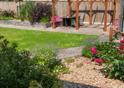 Well-maintained garden with green lawn, paved pathway, flower borders and wooden fencing in a residential care setting.