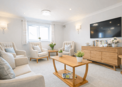 Bright communal lounge with armchairs, coffee table, television and soft furnishings creating a homely setting.